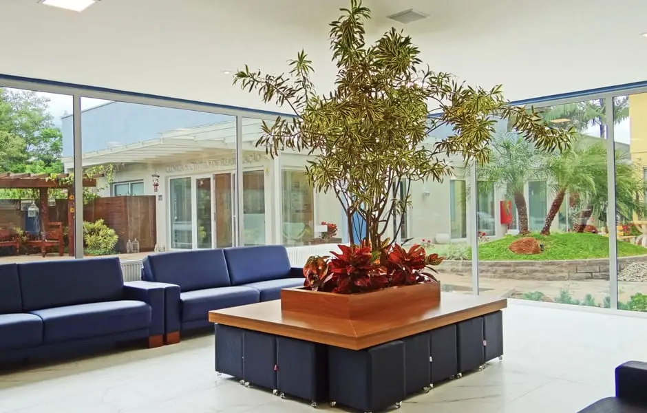 Sala de estar da recepção do Serraville com sofás e jardim interno envidraçado